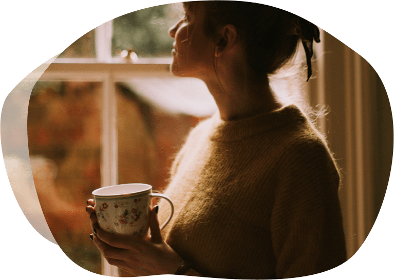 Dame står med kaffekoppen i vinduet